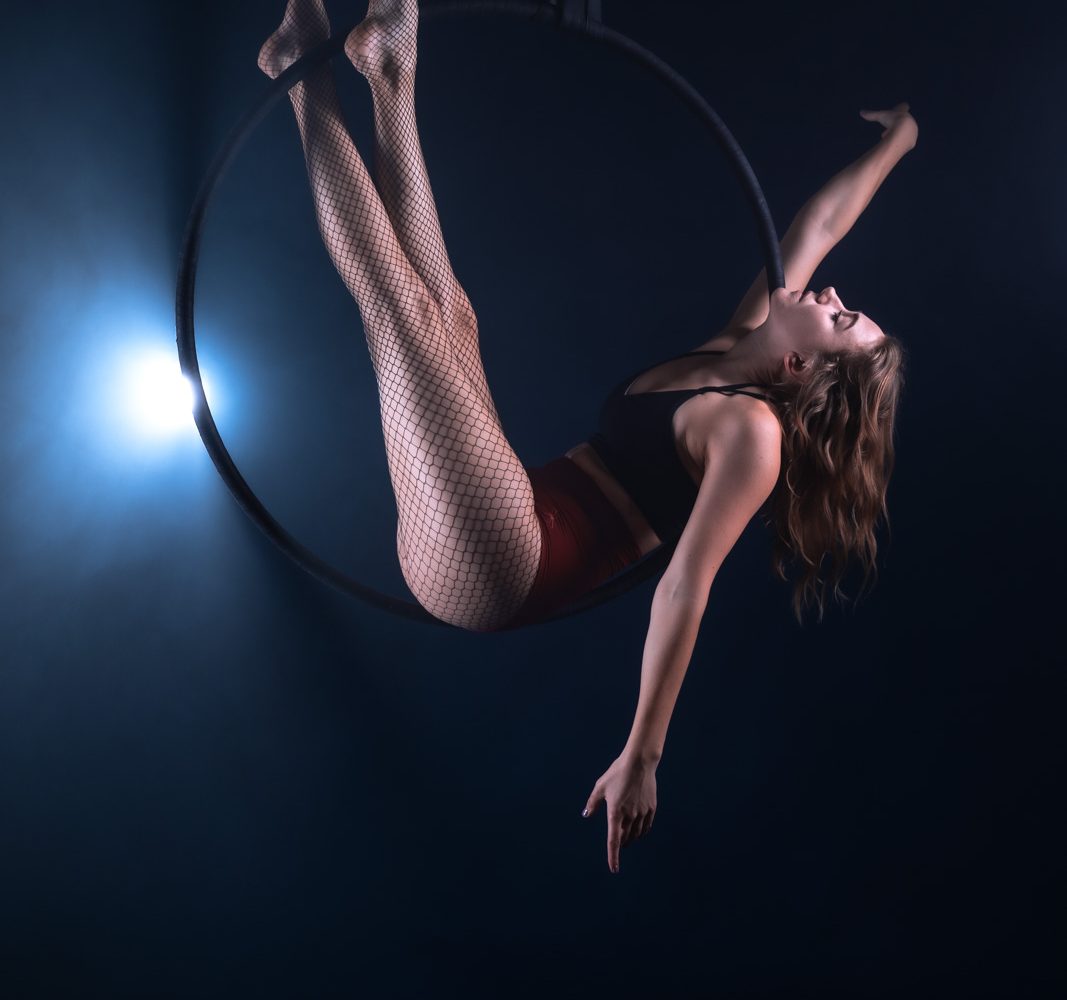Aerial-Hoop Akrobatin vor dunklem Hintergrund im Scheinwerferlicht.
