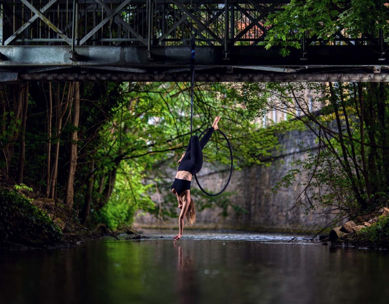 Aerial-Hoop Fotografie an einer Brücke über einem Fluss. Turnerin in akrobatischer Pose wird fotografiert.