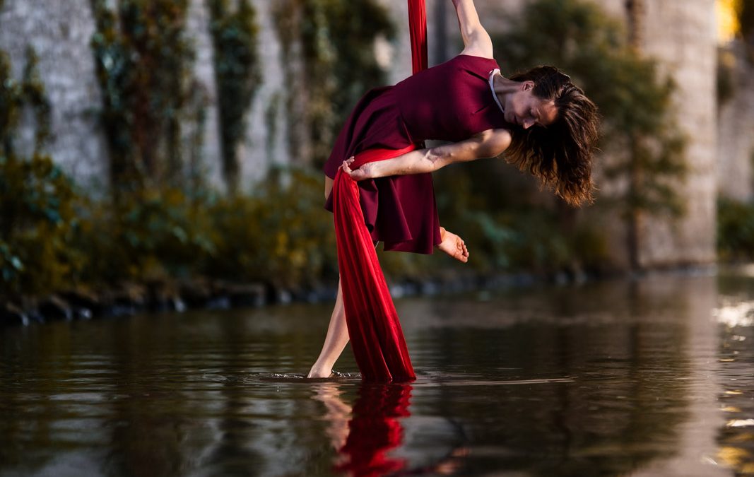 Artistin turnt an roten Tüchern über einem Fluss.