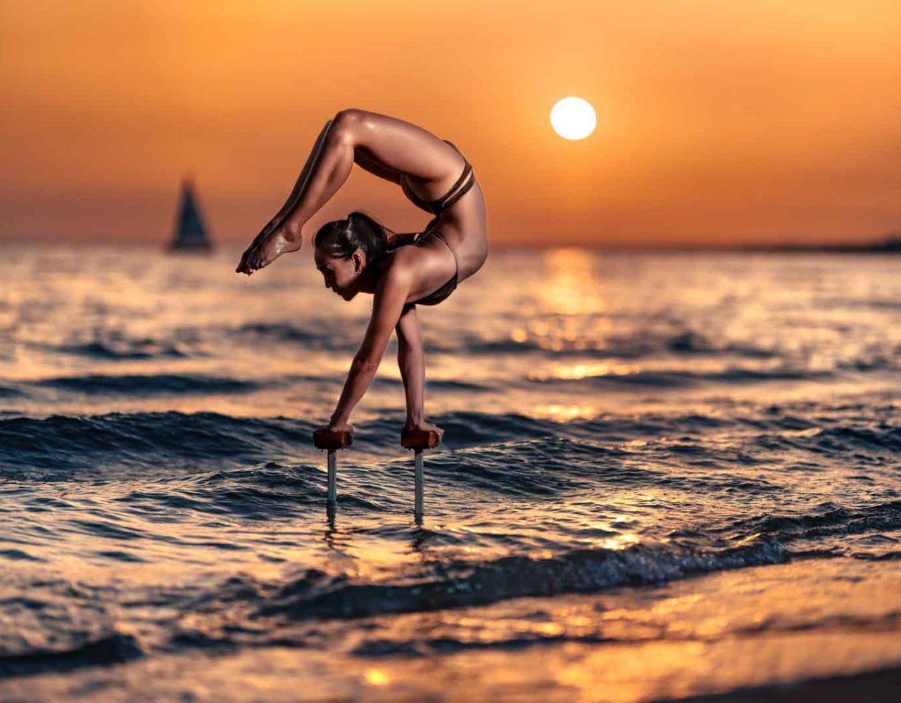 Zirkus-Artistin steht auf Stäben im Wasser im Handstand.