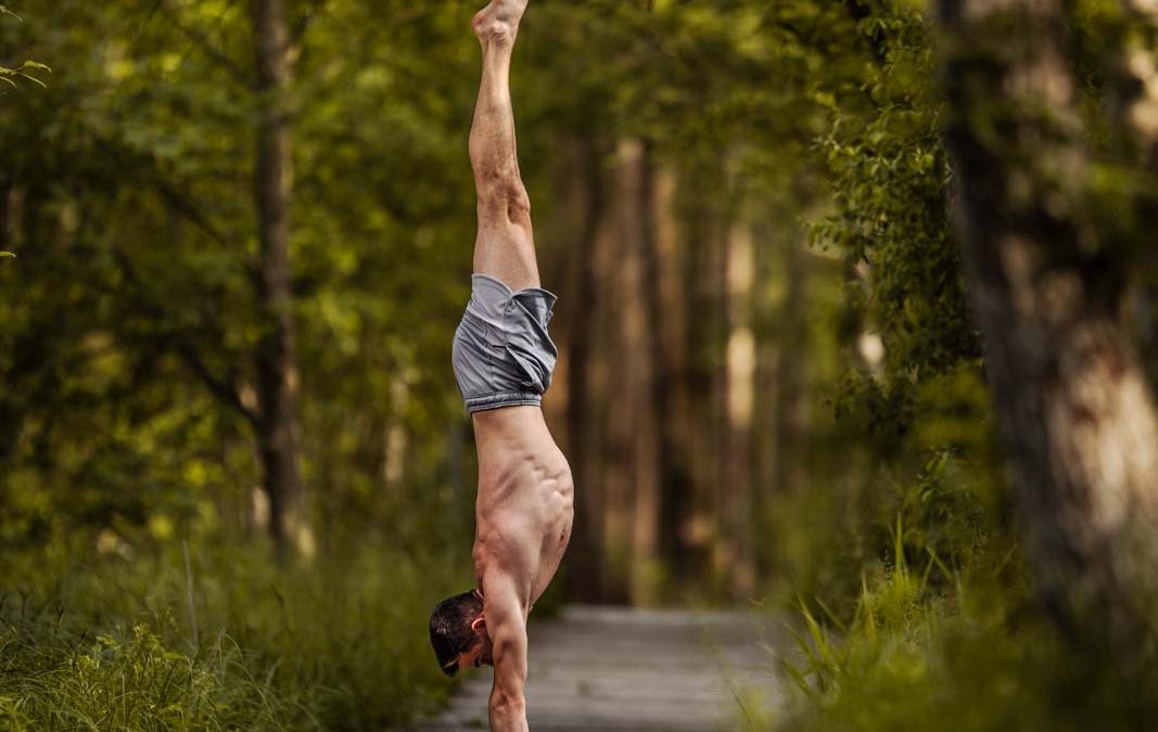 Handstand-Fotografie: Mann steht im geraden Handstand auf einem Weg im Wald.