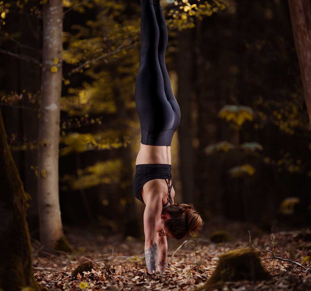 Yoga-Fotografie: Frau steht im Handstand auf einer Lichtung im Wald bei München..