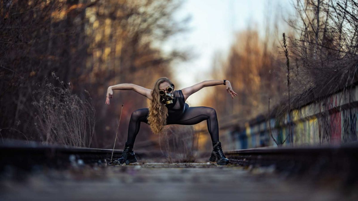Steampunk Fantasy-Fotoshooting: Frau in bedrohlicher Pose auf stillgelegten Bahnschienen trägt eine Steampunk-Maske.