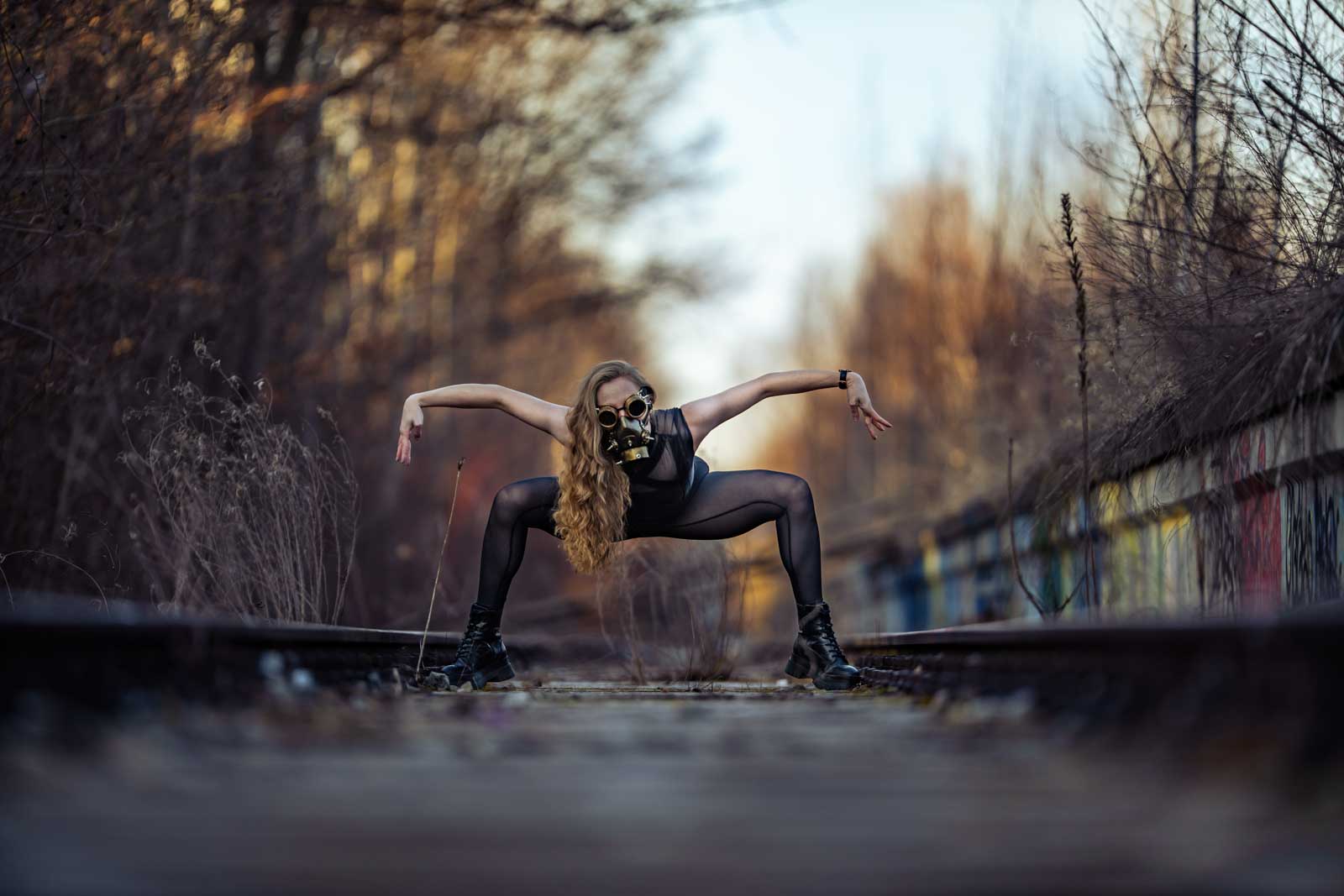 Steampunk Fantasy-Fotoshooting: Frau in bedrohlicher Pose auf stillgelegten Bahnschienen trägt eine Steampunk-Maske.