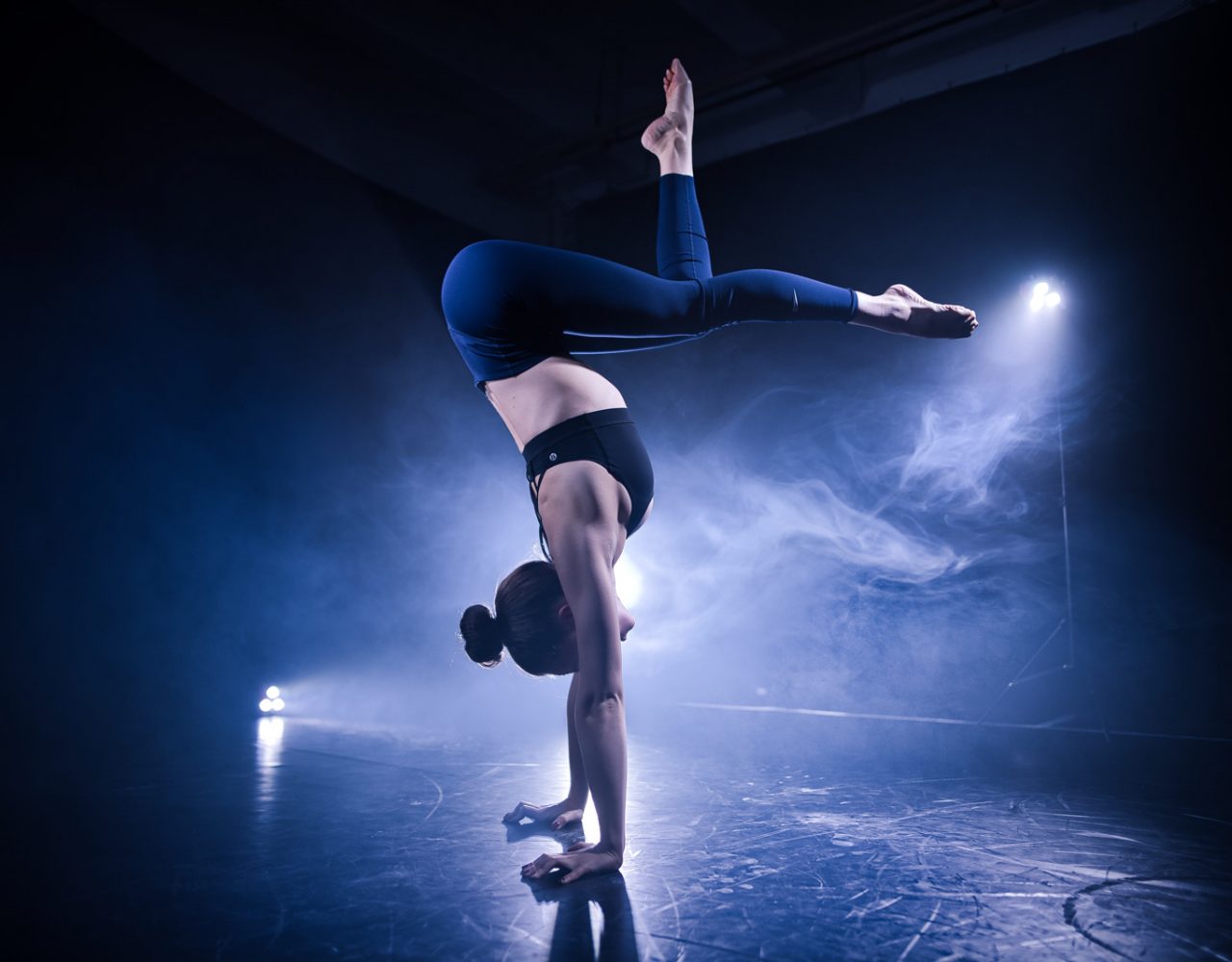 Akrobatin im Handstand auf der Bühne im Scheinwerferlicht mit Nebel im Hintergrund