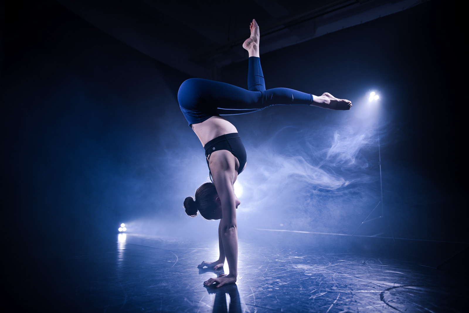 Akrobatin im Handstand auf der Bühne im Scheinwerferlicht mit Nebel im Hintergrund
