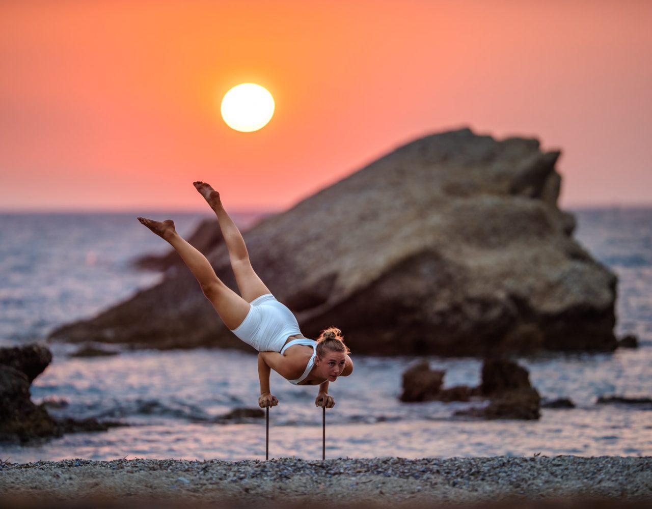 Frau auf Handstand-canes vor Felsen im Meer im Sonnenuntergang.