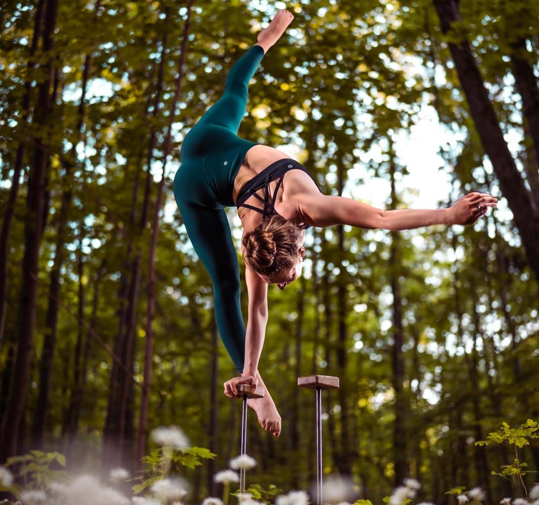 Handstand-Akrobatin biegt sich im Handstand zur Seite. Sie steht auf Metallstäben im Wald.