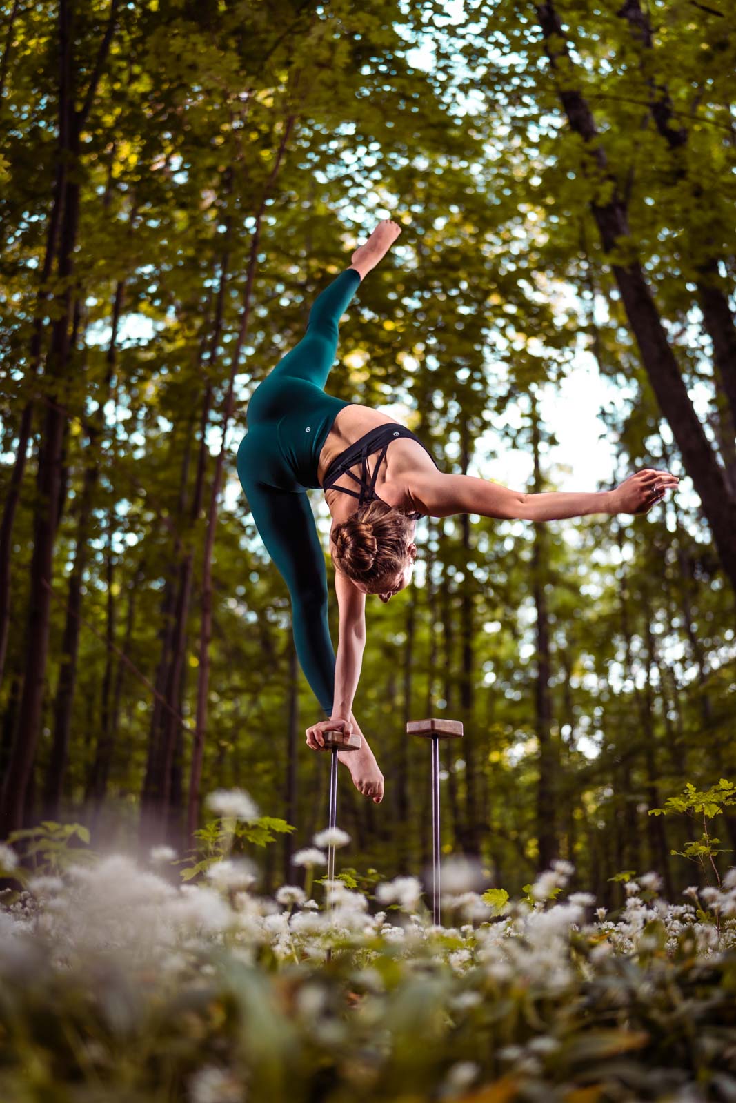 Handstand-Akrobatin biegt sich im Handstand zur Seite. Sie steht auf Metallstäben im Wald.