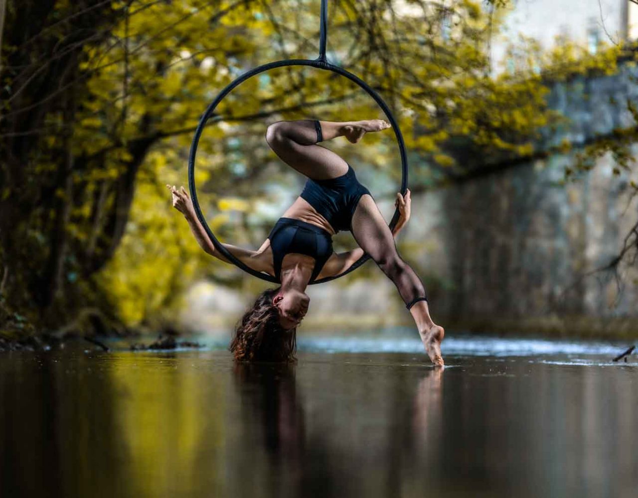 Frau hängt über Kopf im Aerial Hoop über einem Fluss.