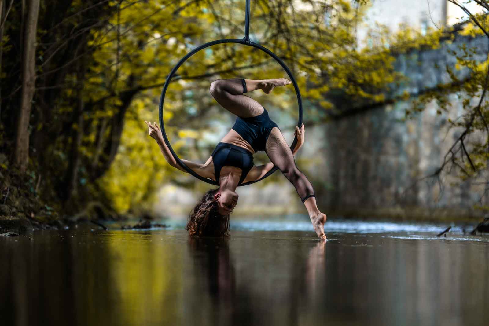 Frau hängt über Kopf im Aerial Hoop über einem Fluss.