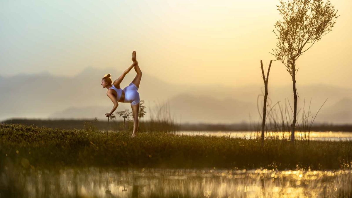 Taenzerin in eleganter Pose auf einem Bein auf einer Wiese am See.