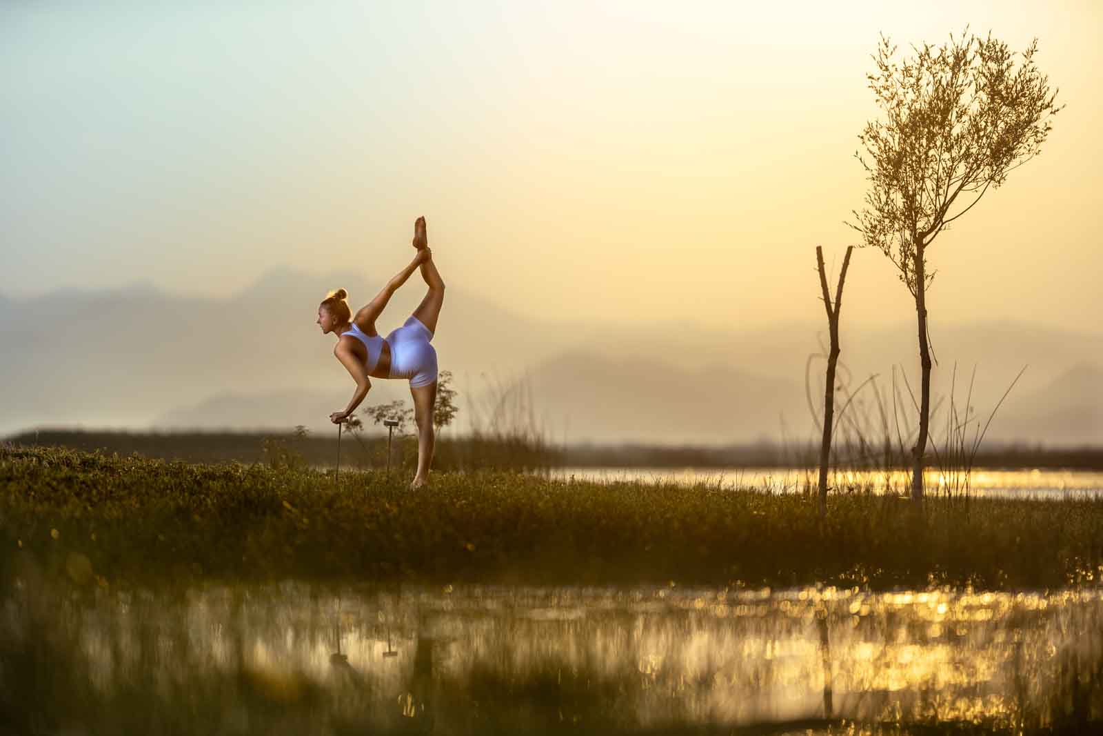 Yoga Fotografie: Taenzerin in eleganter Yoga Pose auf einem Bein auf einer Wiese am See.