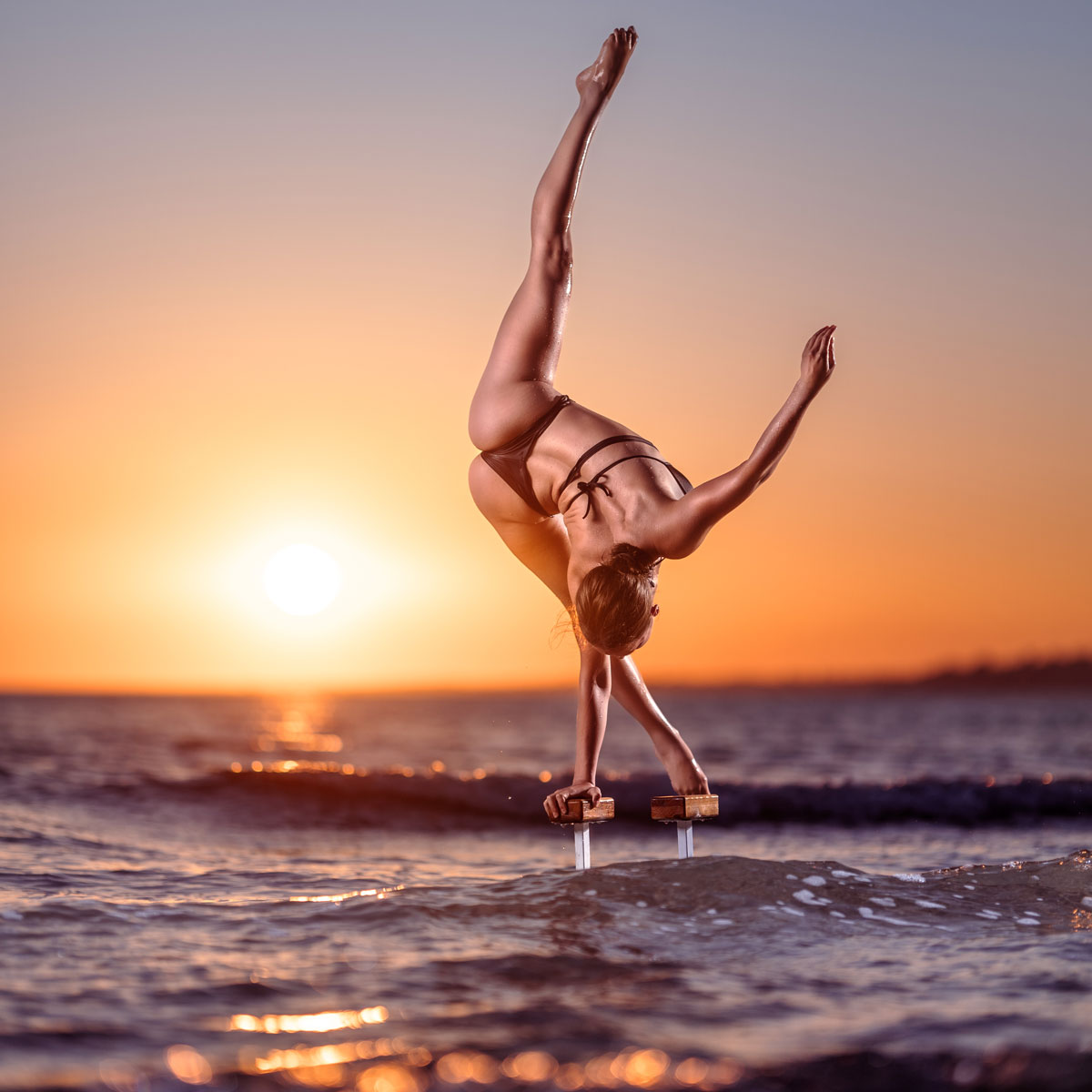 Akrobatikfotografie: Artistin steht im einarmigen Handstand im Sonnenuntergang