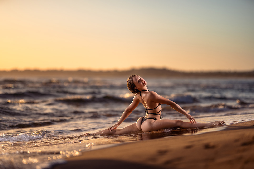 Frau im Bikini macht Spagat im Sonnenuntergang.